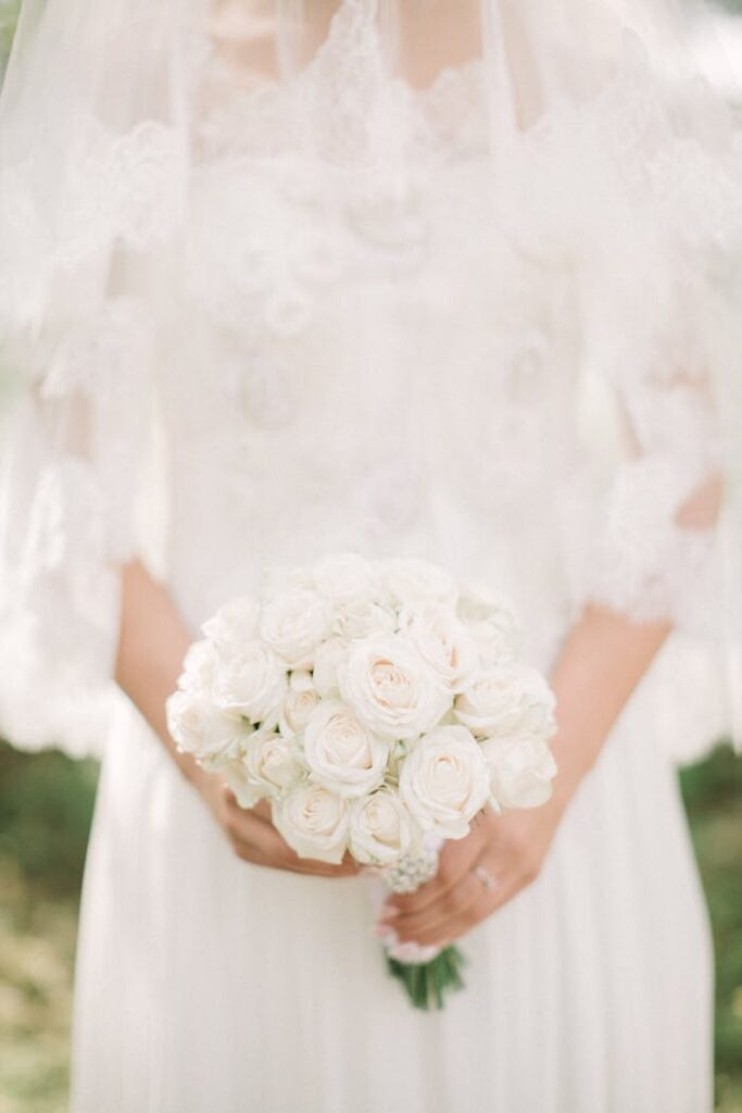 Braut im eleganten Spitzenkleid mit einem Strauß weißer Rosen bei ihrer freien Trauung