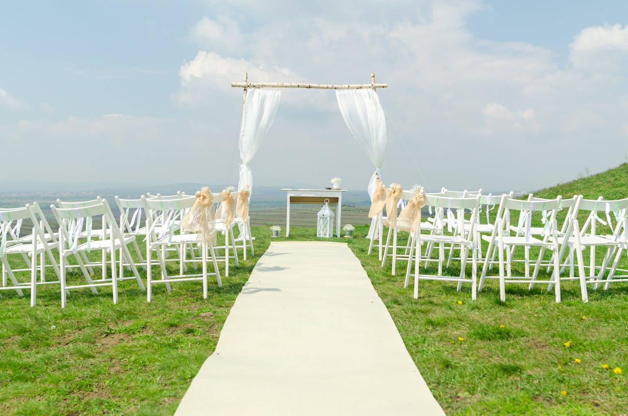 Elegant outdoor wedding setup with chairs and arch under a blue sky.